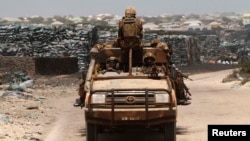 Kenya Defense Force (KDF) soldiers, serving in the African Union Mission in Somalia (AMISOM), patrol past stockpiles of charcoal near the Kismayo sea port town in lower Juba region, Somalia, Feb. 27, 2013.