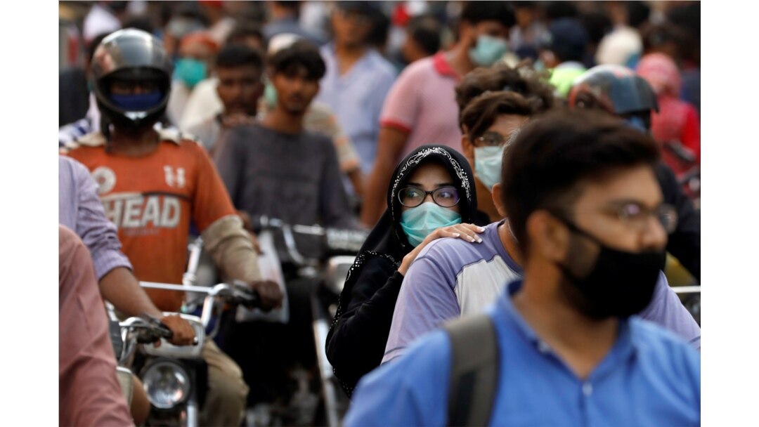 seorang wanita mengendarai sepeda motor saat dia mengenakan masker pelindung di tengah serbuan orang di luar pasar ketika wabah penyakit coronavirus (COVID-19) berlanjut, di Karachi, Pakistan 8 Juni 2020