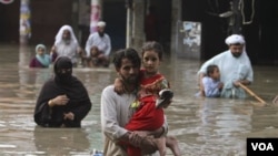 Keluarga di sebuah desa di Karachi, Pakistan harus menyeberangi banjir yang menggenangi desa mereka (10/9).