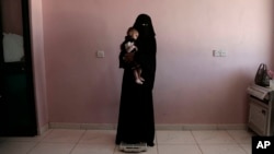 Umm Mizrah, a 25-year-old Yemeni woman, holds her son Mizrah on a scale in Al-Sadaqa Hospital in the southern Yemen city of Aden, Feb. 13, 2018. 