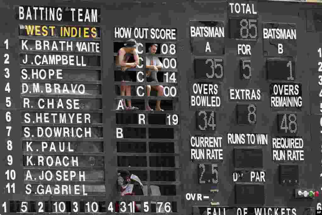 Standing on the scoreboard, people watch day four of the third cricket Test match between England and West Indies, at the Daren Sammy Cricket Ground in Gros Islet, St. Lucia, February 12, 2019.