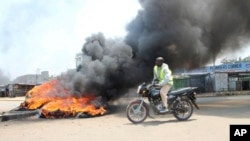 A motorcycle rider passes burning tires blocking a road in the Kondele area of Kisumu, Kenya, during protests in support of Kenyan opposition leader and presidential candidate Raila Odinga, Aug. 9, 2017.