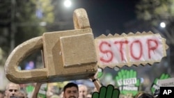 FILE - Protesters carrying a mock chainsaw and signs that read "All for the forests" march in Bucharest, Romania, Nov. 3, 2019. 