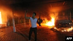 An armed man waves his rifle as buildings and cars are engulfed in flames after being set on fire inside the U.S. consulate compound in Benghazi late on September 11, 2012.