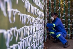 Silva Cossa, juru kunci, mengikat pita ke pagar untuk mewakili seorang Afrika Selatan yang meninggal dunia karena COVID-19, di gereja St James Presbyterian di Bedford Gardens, Johannesburg, Afrika Selatan, 29 Juli 2020..