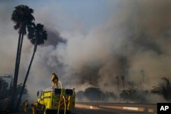 Firefighters battle a wildfire as smoke rises from burning palm trees at Faria State Beach in Ventura, California, Dec. 7, 2017.
