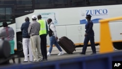 A Zimbabwean national, centre, is escorted to the bus by a police upon his arrival upon arrival at Robert Mugabe International airport in Harare, Thursday, July 22, 2021. 