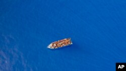 FILE - A group thought to be migrants from Tunisia on board a precarious wooden boat waits to be assisted by a team of the Spanish NGO Open Arms, around 20 miles southwest from the Italian island of Lampedusa, July 29, 2021. 