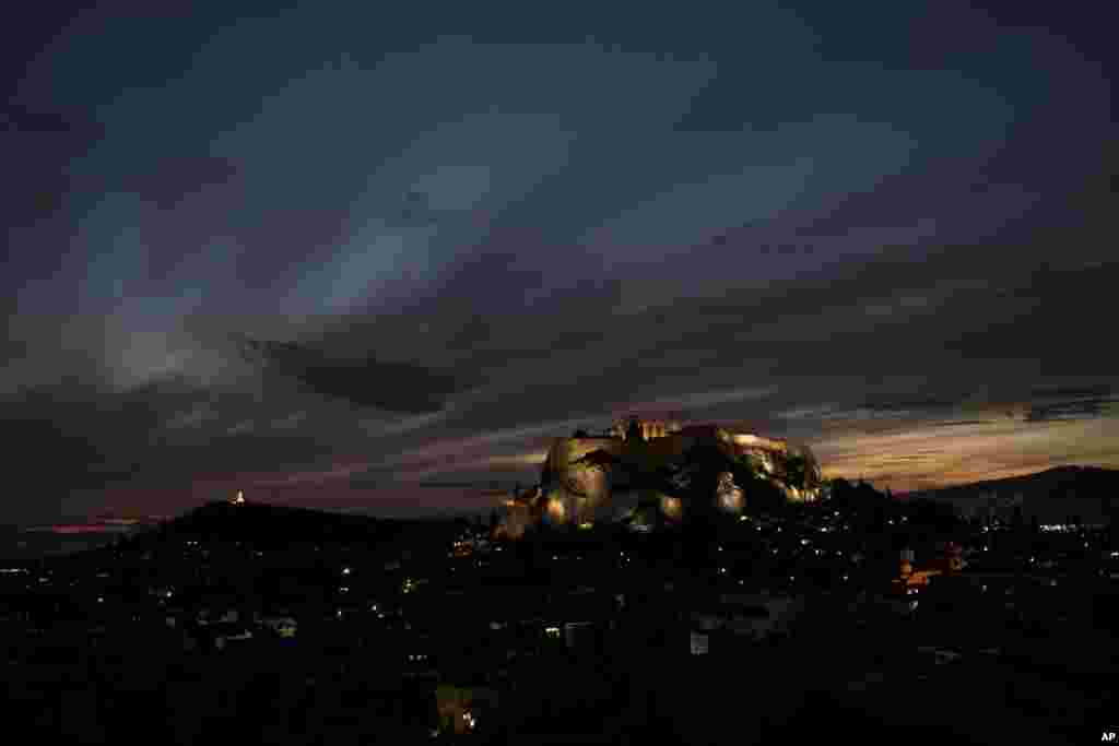 The sun sets behind the ancient Acropolis hill and the ruins of the fifth century B.C. Parthenon temple in Athens, Greece.