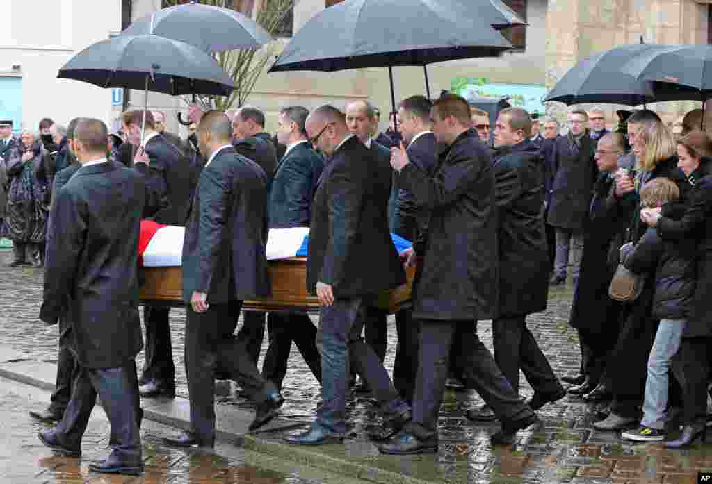 French Interior Minister Bernard Cazeneuve (at right, under umbrella) attends the funeral of police officer Franck Brinsolaro, at the Sainte Croix church, in Bernay, western France, Jan. 15, 2015.