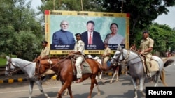 La police patrouille sur des chevaux devant une affiche avec l’image du Premier ministre Narendra Modi Inde, du président Xi Jinping de la Chine et du ministre en chef de l'État indien de Gujarat Anandiben Patel, à Ahmedabad, Inde, 16 septembre 2014.