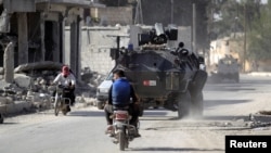 FILE - Men ride motorbikes past a Turkish armored carrier in the northern Syrian rebel-held town of al-Rai, in Aleppo Governorate, Syria, Oct. 5, 2016.