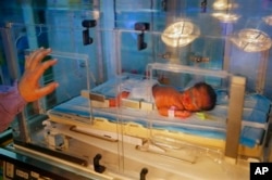 FILE - Ahed Hussein, 18, a Syrian refugee who fled the war in Syria, puts her hand on the incubator where her premature newborn daughter rests in Chtaura's hospital in Chtaura, Lebanon.