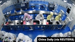 FILE PHOTO: Employees work on a production line manufacturing camera lenses for cellphones at a factory in Lianyungang, Jiangsu province, China April 30, 2019. 