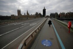 FILE - People pass over a quiet Westminster Bridge, backdropped by the scaffolded Houses of Parliament and the Elizabeth Tower, known as Big Ben, in London, during England's third coronavirus lockdown, March 23, 2021.