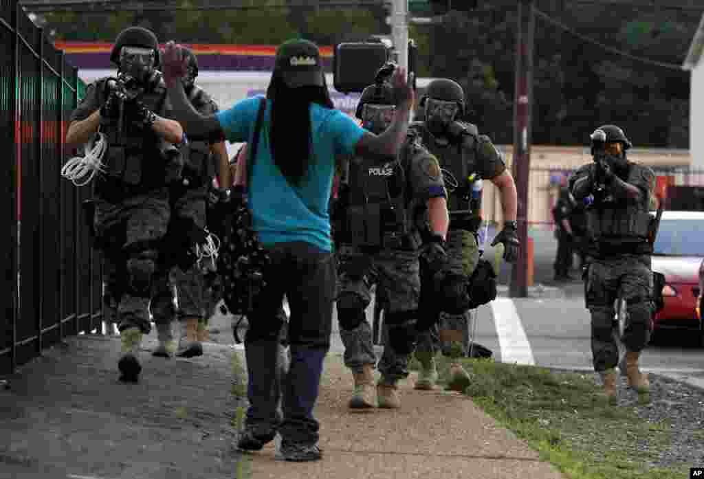 Police wearing riot gear walk toward a man with his hands raised in Ferguson, Missouri, USA, Aug.11, 2014. Authorities have made several arrests in Ferguson, where crowds have looted and burned stores, vandalized vehicles and taunted police after a vigil for an unarmed black man who was killed by police.