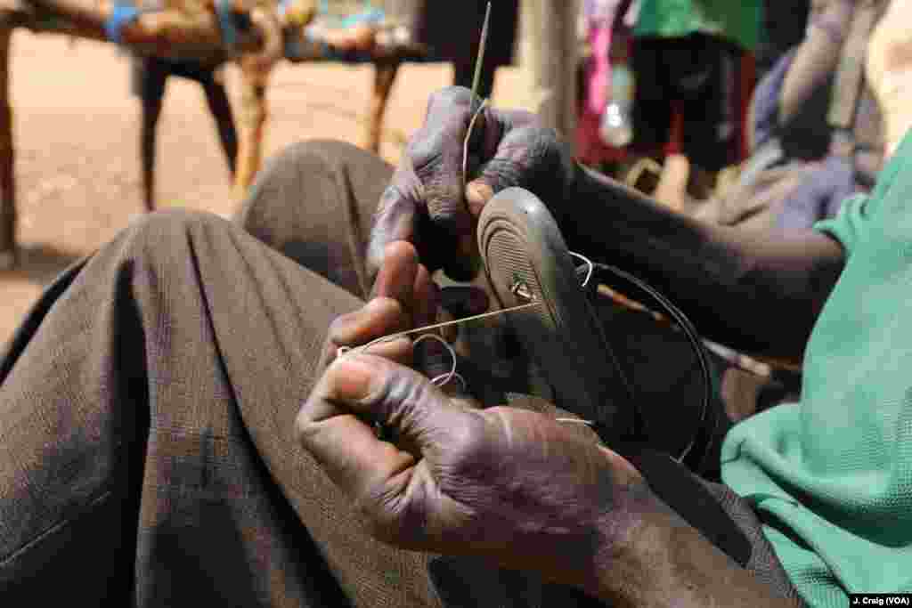 جنوبی سوڈان سے تعلق رکھنے والا ایک پناہ گزین اپنی جوتی کی مرمت کر رہا ہے۔