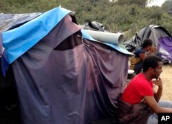 FILE - People sit by a tent at a makeshift camp in Calais, Sept. 7, 2014.