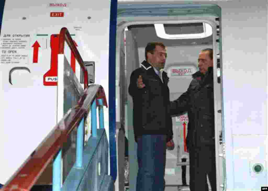 Italian Prime Minister Silvio Berlusconi, right, and Russian President Dmitry Medvedev, back, examine a new Russian passenger plane, Sukhoi Superjet 100, at the airport in the Black Sea resort of Sochi, southern Russia, Friday, Dec. 3, 2010. Italian