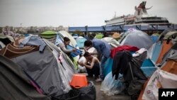 A man cuts another man's hair outside a passenger terminal used as a shelter for refugees and migrants at the Piraeus harbour in Athens on April 3, 2016. 