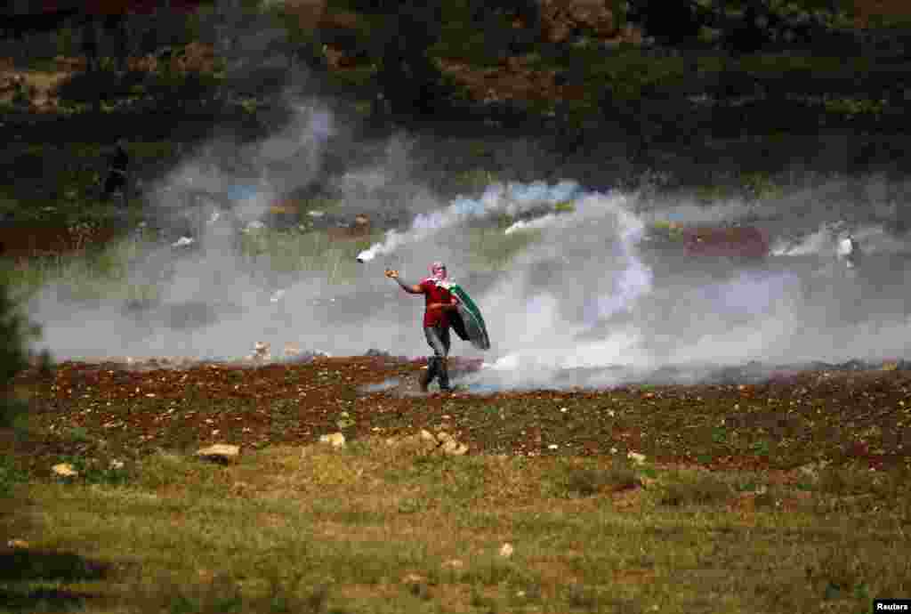 A Palestinian demonstrator returns a tear gas canister toward Israeli security forces during clashes near the West Bank city of Ramallah to mark 65 years since what they call the Nakba (Catastrophe) when Israel&#39;s creation caused many to lose their homes and become refugees. 