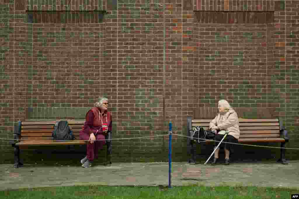 Two women observe social distancing measures as they speak to each other from adjacent park benches amidst the novel coronavirus COVID-19 pandemic, in the center of York, northern England, March 19, 2020.