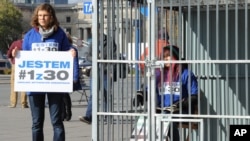 A Greenpeace activist sits in a cage and another one holds a placard reading "I am 1of the 30" in a protest against the imprisonment of Greenpeace activists in Russia, in downtown Warsaw, Poland, Oct. 2, 2013. 