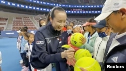 Chinese tennis star Peng Shuai signs large-sized tennis balls at the opening ceremony of Fila Kids Junior Tennis Challenger Final in Beijing, China, Nov. 21, 2021, in this screen grab obtained from a social media video. (Twitter @QINGQINGPARIS via Reute