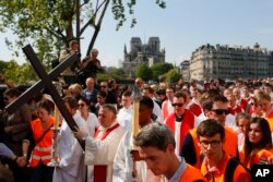 With the Notre Dame cathedral in background, religious officials carry the cross during the Good Friday procession, April 19, 2019, in Paris. French art conservation officials say the works inside Notre Dame suffered no major damage in this week's fire.