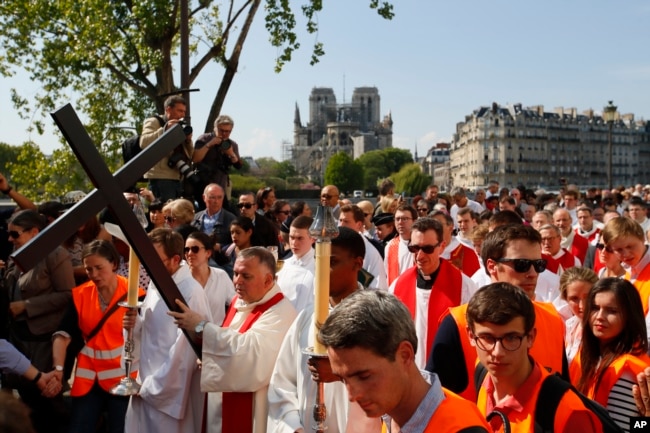 With the Notre Dame cathedral in background, religious officials carry the cross during the Good Friday procession, April 19, 2019, in Paris. French art conservation officials say the works inside Notre Dame suffered no major damage in this week's fire.