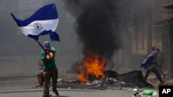 A masked protester waves a Nicaraguan national flag in front of a burning barricade, as protesters clashed with riot police in the Monimbo district of Masaya, Nicaragua, May 12, 2018.