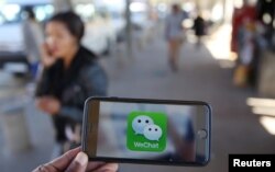 FILE - A WeChat logo is displayed on a mobile phone as a woman walks past, July 21, 2016.