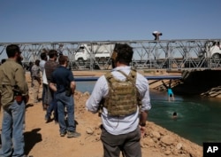 U.S. soldiers in civilian clothes, foreground, watch boys diving into a canal from a newly opened bridge, which had been destroyed last summer during fighting between U.S.-backed Syrian Democratic Forces fighters and Islamic State militants, in Raqqa, Syr