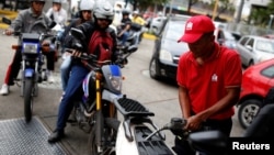 A gas station worker pumps gas into a motorcycle as people wait in line to fill the tanks of their vehicles at a gas station of the state oil company PDVSA in Caracas, Venezuela, March 22, 2017. 