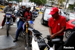 FILE - A worker pumps gas into a motorcycle as people wait in line to fill their vehicles' tanks at a state-owned PDVSA station in Caracas, Venezuela in March.