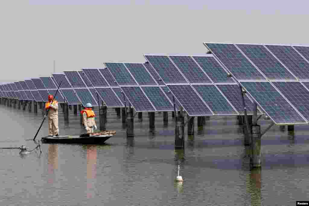 Para pekerja memeriksa papan panel surya di kota Lianyungang, Jiangsu, China.