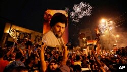 FILE - Supporters of Shiite cleric Muqtada al-Sadr, carry his image as they celebrate in Tahrir Square, Baghdad, Iraq, May 14, 2018. 