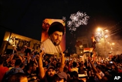 FILE - In this Monday, May 14, 2018 file photo, supporters of Shiite cleric Muqtada al-Sadr, carry his image as they celebrate in Tahrir Square, Baghdad, Iraq.