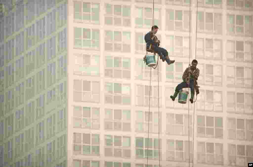 Window washers use cables to lower themselves from a skyscraper while working on a polluted day in Beijing, China.