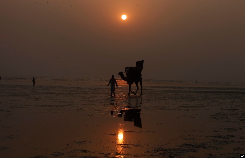 Un hombre pakistaní y su camello se siluetean contra el último atardecer de 2016 en la playa de Clifton en Karachi, Pakistán. (Foto AP)