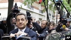 French President and UMP party candidate for the elections Nicolas Sarkozy, left, prepares to enter a car as he leaves his campaign headquarters the morning after the first round of voting in Paris, April 23, 2012. 