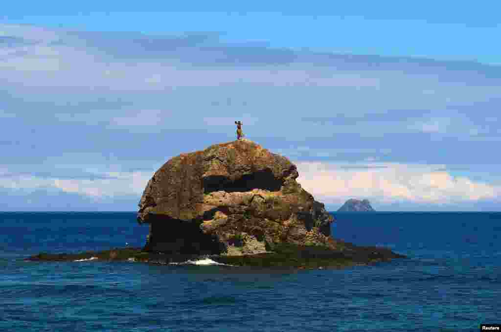 A man dressed as a traditional Fijian warrior stands atop a rock as tourists arrive by ferry on Barefoot Kuata Island, located in the Yasawa Islands that are part of the South Pacific nation of Fiji.