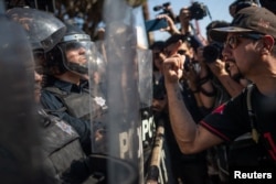 A demonstrator, part of a protest march against migrants, shouts towards a line of police in riot gear who were standing guard over a temporary shelter housing a caravan from Central America, in Tijuana, Mexico, Nov. 18, 2018.