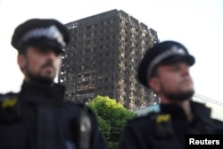 Police officers stand in front of the The Grenfell Tower block that was destroyed by fire, in north Kensington, West London, Britain, June 16, 2017.