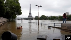 FILE - In this June 4, 2016, file photo, a woman, at right, takes photos of the flooded banks of the Seine in Paris. Scientists said at the time that man-made climate change had nearly doubled the likelihood of April 2016's devastating French flooding.