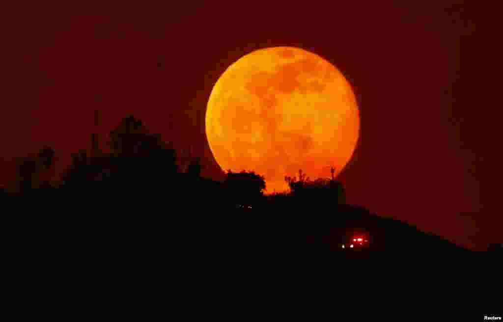 An emergency vehicle makes its way past a rising moon as it travels along a burned-out hillside near San Marcos, California, May 14, 2014.