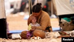 A refugee woman from the minority Yazidi sect, who fled the violence in the Iraqi town of Sinjar, sits with a child inside a tent at Nowruz refugee camp in Qamishli, northeastern Syria, Aug. 17, 2014. 