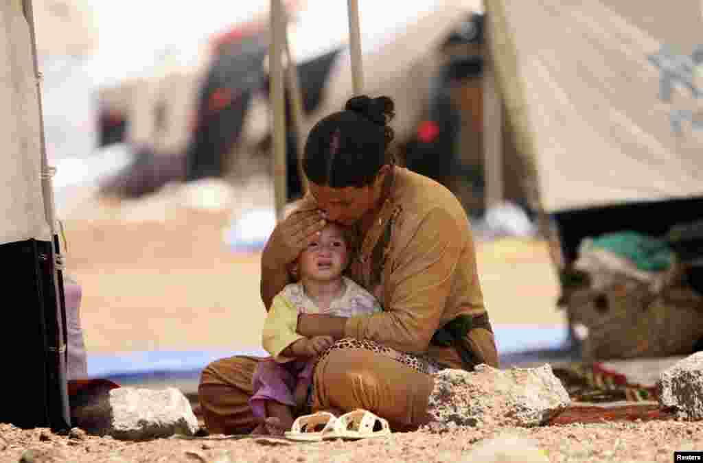 Seorang pengungsi perempuan dari sekte minoritas Yazidi, yang menungsi dari kekerasan di kota Sinjar di Irak, duduk bersama anaknya dalam tenda di kamp pengungsi Nowruz di Qamishli, timur laut Suriah (17/8). (Reuters/Rodi Said)