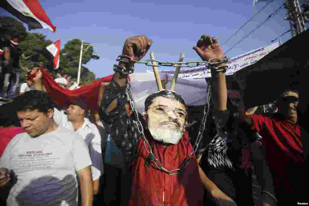 A protester opposing Egyptian President Mohamed Morsi wears a defaced poster of Morsi as a mask in front of the presidential palace in Cairo, June 30, 2013. 