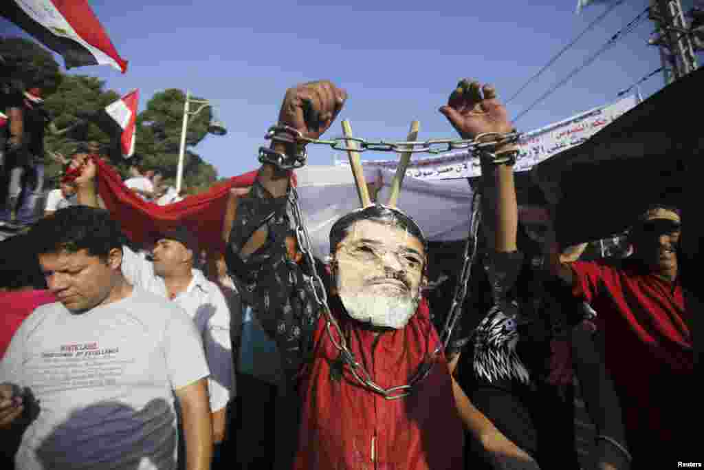 A protester opposing Egyptian President Mohamed Morsi wears a defaced poster of Morsi as a mask in front of the presidential palace in Cairo, June 30, 2013.